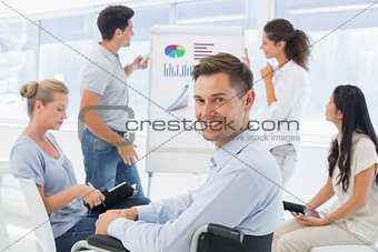Casual businessman in wheelchair smiling at camera during presentation