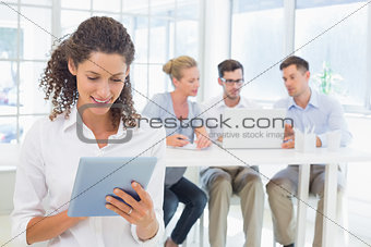 Casual businesswoman using tablet with team behind her