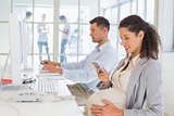 Casual pregnant businesswoman texting on phone at desk