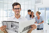 Casual businessman holding newspaper smiling at camera
