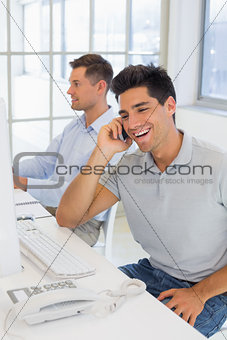 Casual businessman laughing on the phone at his desk
