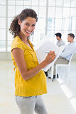 Casual pregnant businesswoman writing in folder smiling at camera