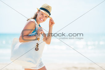 Portrait of smiling young woman in hat with bag on beach
