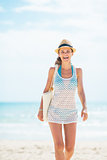 Happy young woman in hat with bag walking on beach