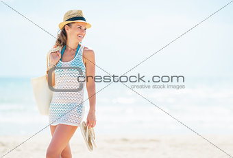 Smiling young woman in hat with bag on beach looking on copy spa