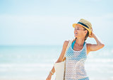 Happy young woman in hat with bag on beach looking on copy space