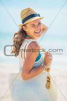 Portrait of smiling young woman in hat with bag on beach