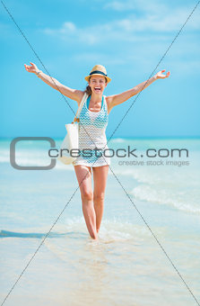 Young woman in hat with bag walking on sea coast and rejoicing