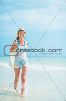 Happy young woman in hat with bag walking on sea coast