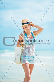 Happy young woman in hat with bag walking on sea coast