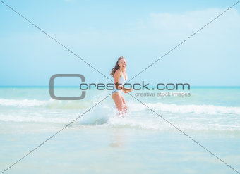 Happy young woman in swimsuit running into sea