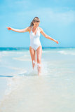 Happy young woman in swimsuit walking on sea shore