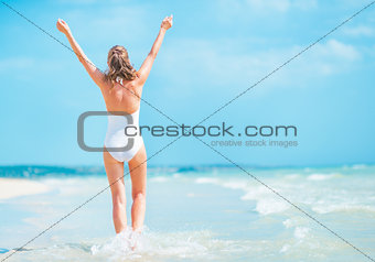 Young woman in swimsuit walking on sea coast. rear view