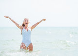 Happy young woman in swimsuit standing in sea and rejoicing