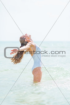 Happy young woman in swimsuit standing in sea and rejoicing