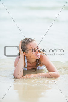 Happy young woman in swimsuit laying on sea shore