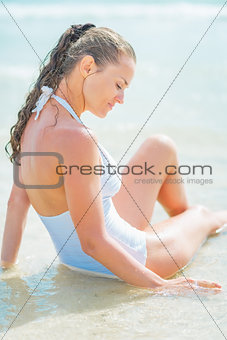 Happy young woman in swimsuit sitting on sea shore