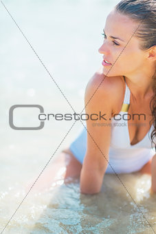 Young woman in swimsuit sitting at seaside and looking into dist