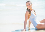 Happy young woman in swimsuit sitting on sea shore and looking o