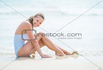 Happy young woman in swimsuit sitting on sea coast