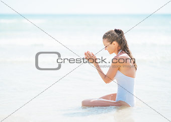 Happy young woman in swimsuit sitting at seaside and playing wit