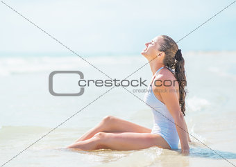 Relaxed young woman in swimsuit sitting in water at seaside