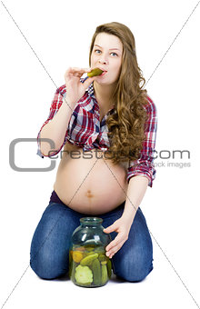 Pregnant young woman on a white background eats pickled cucumber