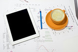 Tablet pc, cup of coffee and paper with graphs