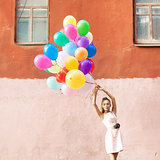 beautiful lady in retro outfit holding a bunch of balloons betwe