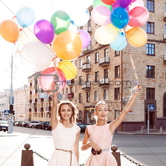 two beautiful ladys in retro outfit holding a bunch of balloons 