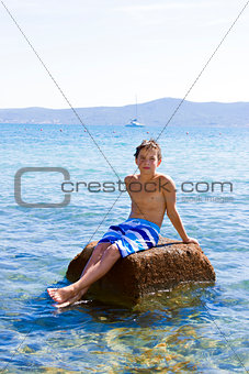 Cute eleven years old boy sitting on a rock in the sea