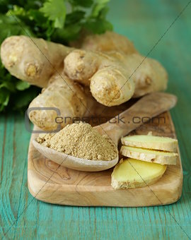 ground ginger in a wooden spoon, fresh root in the background