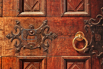Closeup of old ornate wooden door with a gold door handle in Alba, Italy.