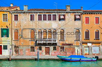 Typical old colorful brick house, wooden shutters on windows and small canal in Venice, Italy.