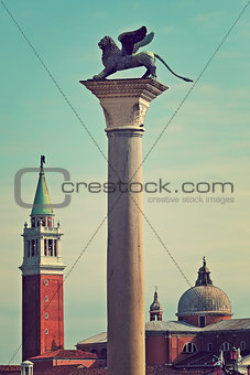 Bronze sculpture of winged lion on column as San Giorgio Maggiore church on background in Venice, Italy (toned, vertical composition).