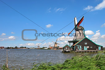 Wooden windmills along river under beautiful blue sky with white clouds in typical dutch village of Zaanse Schans.