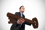 Composite image of businessman carrying large key with arms out