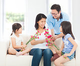 Daughters and father handing mother carnations 