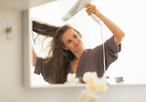 Young woman blow drying hair in bathroom