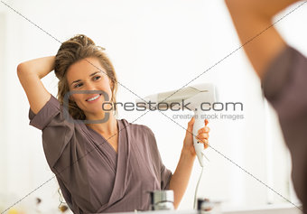 Happy young woman blow drying hair in bathroom