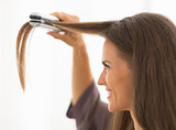 Young woman straightening hair in bathroom