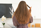 Young woman straightening hair in bathroom. rear view