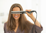 Happy young woman looking through hair straightener