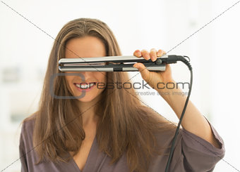Happy young woman looking through hair straightener