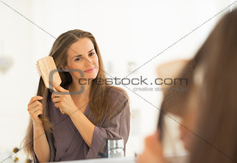 Young woman combing hair in bathroom