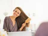 Smiling young woman combing hair in bathroom