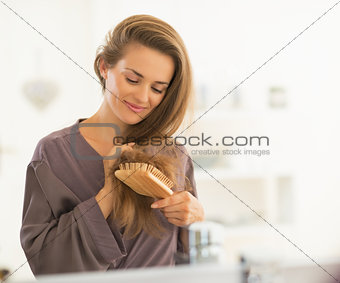 Happy young woman combing hair in bathroom