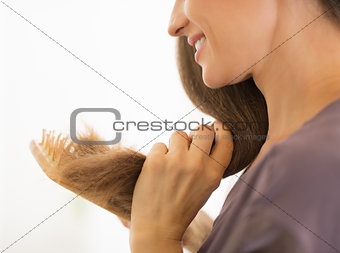 Closeup on happy young woman combing hair in bathroom