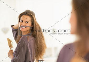 Smiling young woman combing hair in bathroom