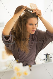 Concerned young woman combing hair in bathroom